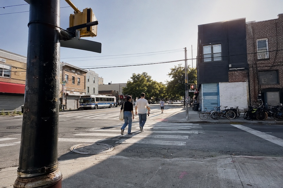 Two friends crossing a neighborhood street in daylight.