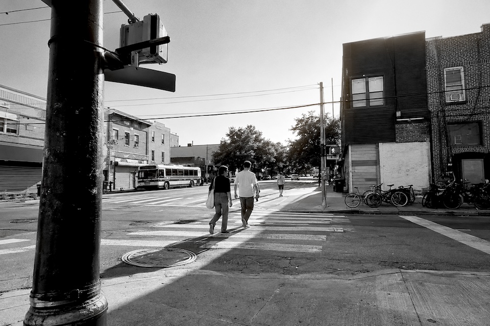 Two friends crossing a neighborhood street in daylight.