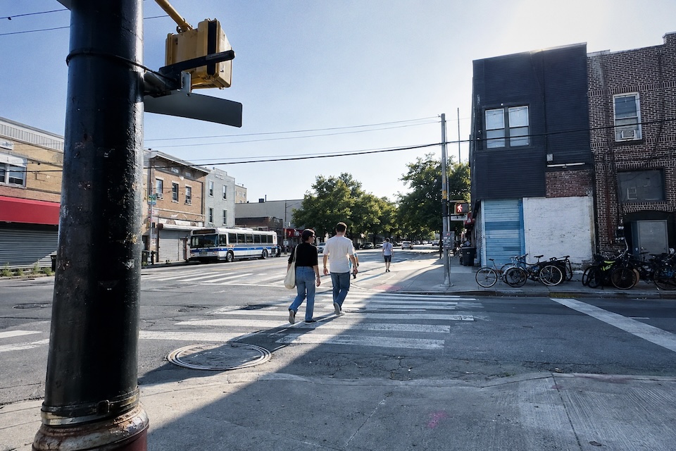 Two friends crossing a neighborhood street in daylight.
