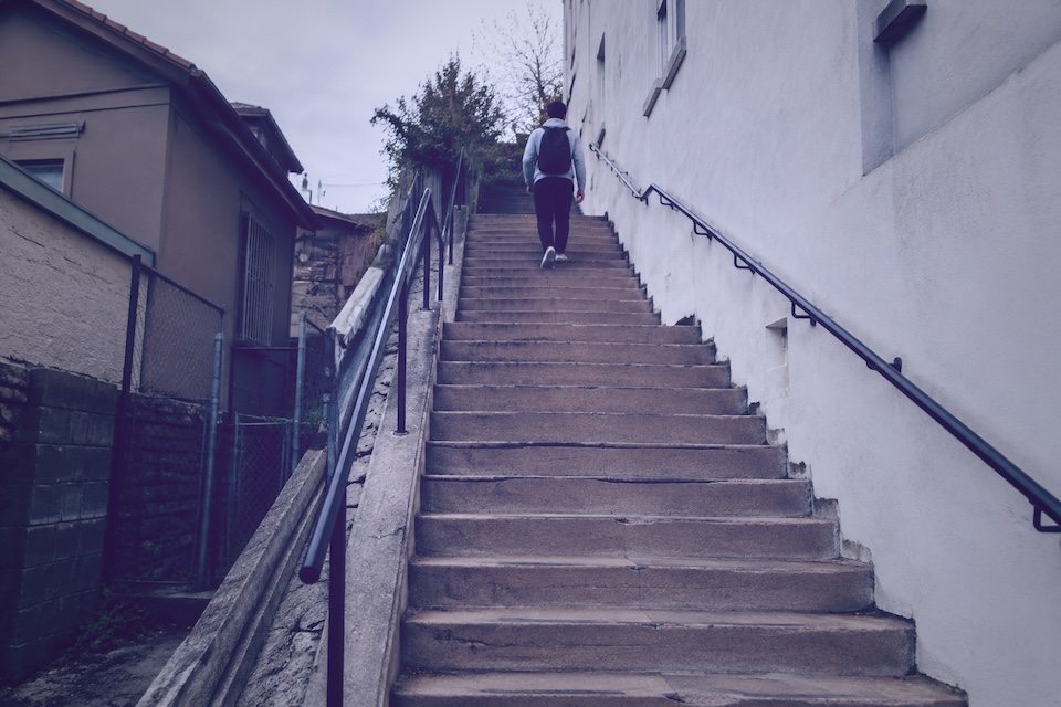 A person with a backpack walking up concrete city steps.