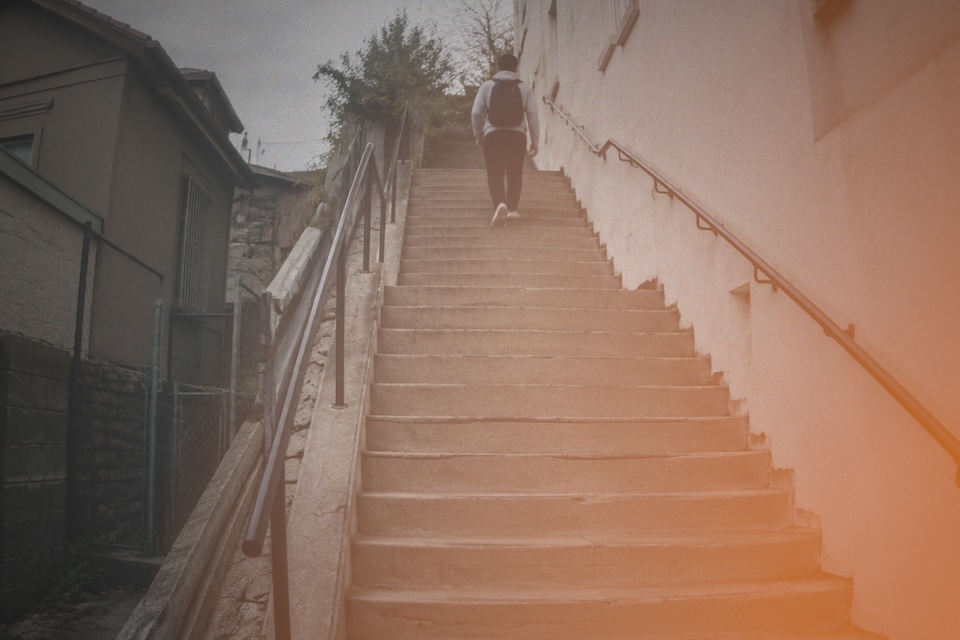 A person with a backpack walking up concrete city steps.