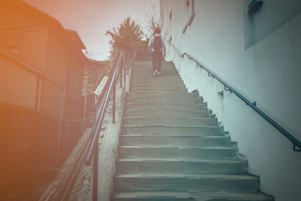 A person with a backpack walking up concrete city steps.