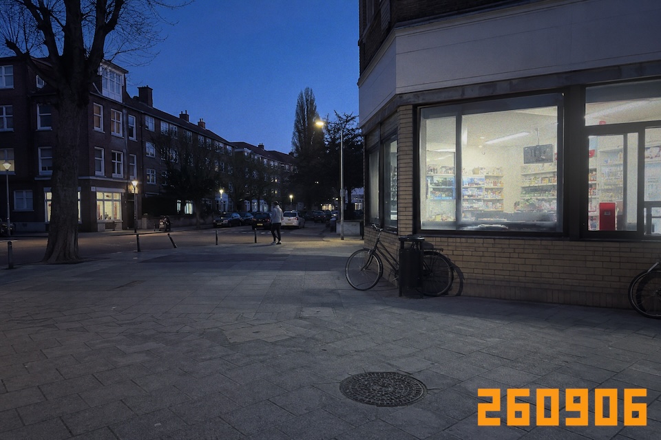 A lit corner shop, bicycles and a passerby at blue hour.