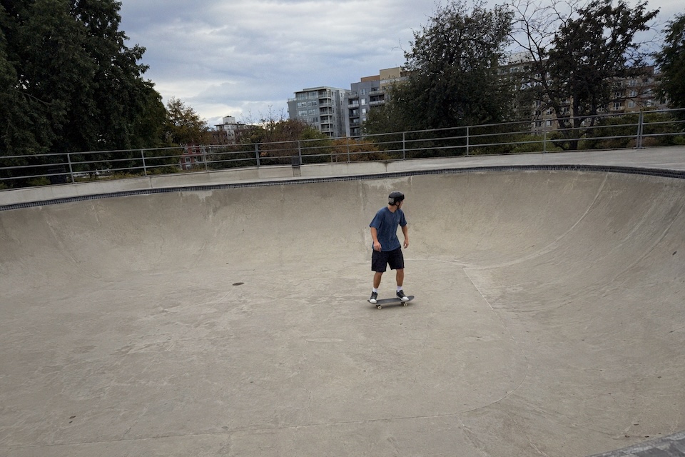 A skateboarder riding across a concrete bowl under an overcast sky.
