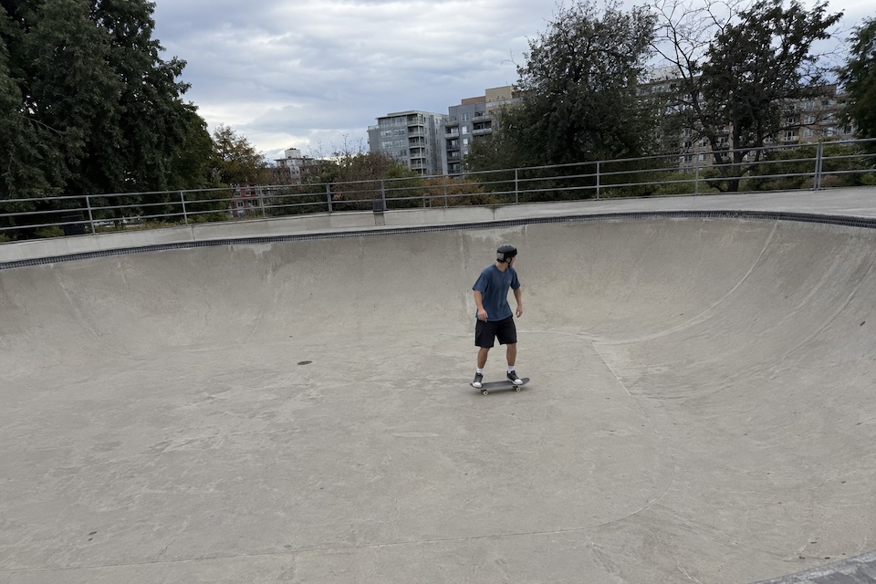 A skateboarder riding across a concrete bowl under an overcast sky. Before processing.