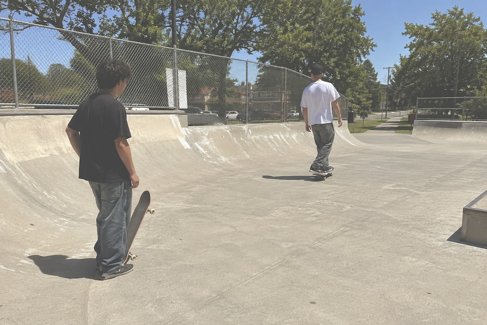 Two skateboarders at a concrete skatepark in daylight.