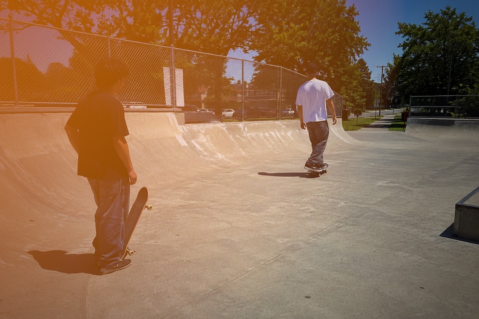 Two skateboarders at a concrete skatepark in daylight.
