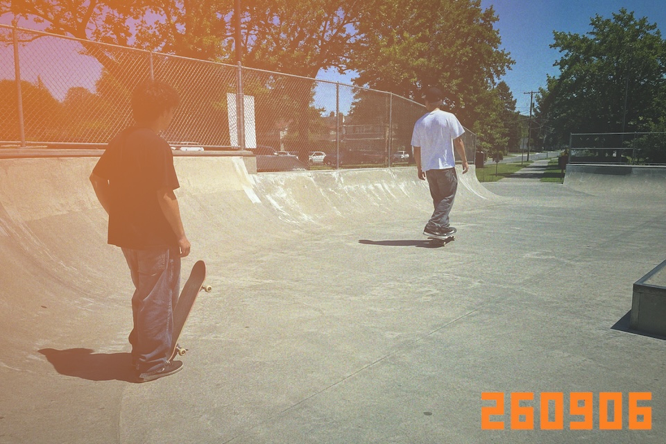 Two skateboarders at a concrete skatepark in daylight.